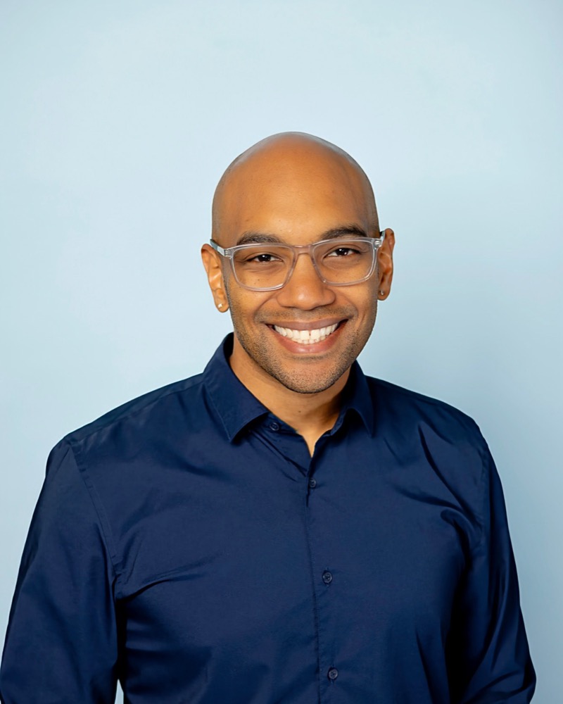 Corey Ashmeade, smiling, in a navy shirt and clear glasses